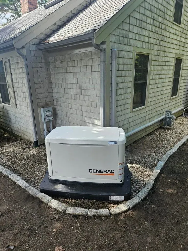 Generac standby generator installed on a paver pad beside a shingle-sided home